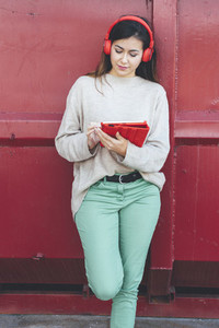 Millennial woman with red headphones using digital tablet with red background