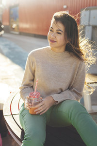 Millennial woman having a break drinking a smoothie seated close to her shopping bags