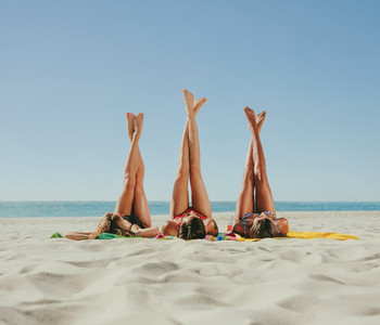 Woman in bikini sunbathing on beach with legs raised to the sky
