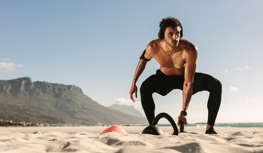 Man doing fitness training at the beach with kettlebells