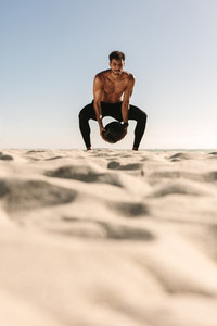 Man training at the beach using a medicine ball