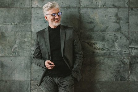 Smiling senior businessman standing on grey wall