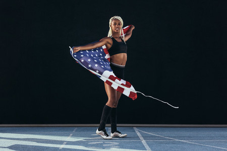 Female athlete walking on running track holding american flag