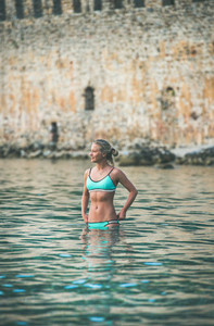 Young woman tourist swimming at beach near ancient fortress wall