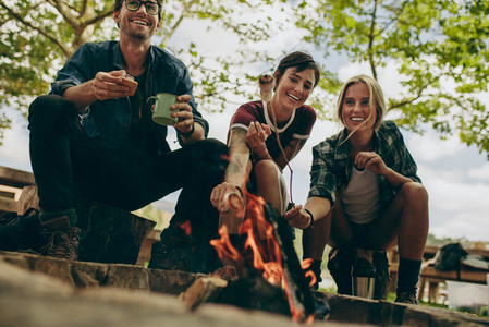Friends camping in the countryside toasting food on bonfire