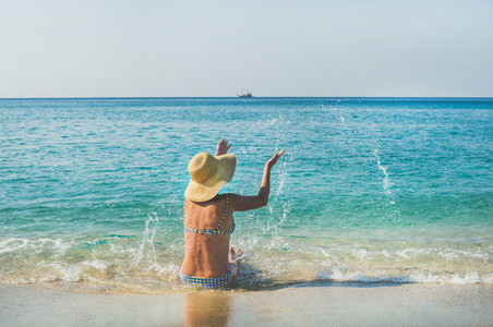 Senior woman tourist in bikini sitting on sand enjoying sea