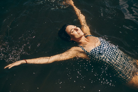 Woman in swimsuit swimming in lake with eyes closed