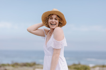 Woman in white gown laughing holding her hat