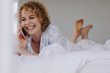 Woman talking on mobile phone lying on bed