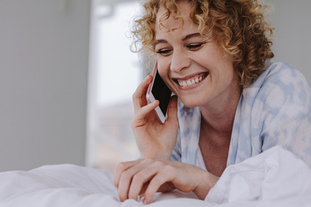 Close up of a smiling woman talking over mobile phone lying on b