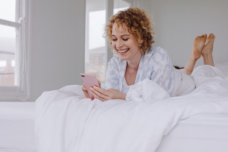 Smiling woman lying on bed looking at her mobile phone