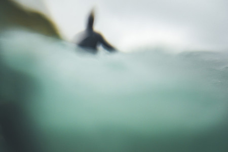 Unfocused back view of a surfer waiting for a wave in a cloudy winter day