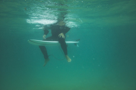 Underwater view of a surfer seated on his board waiting for a wave