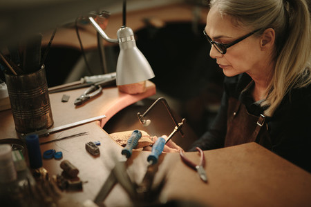 Female jeweler crafting metal in workshop
