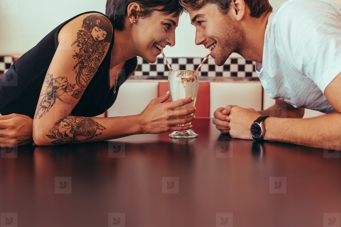 Man and woman sharing milk shake from one glass using straws