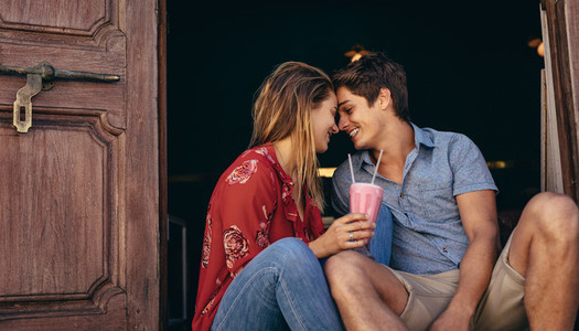 Happy couple sitting outdoors holding a milkshake