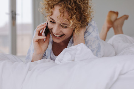 Smiling woman lying on bed talking on mobile phone