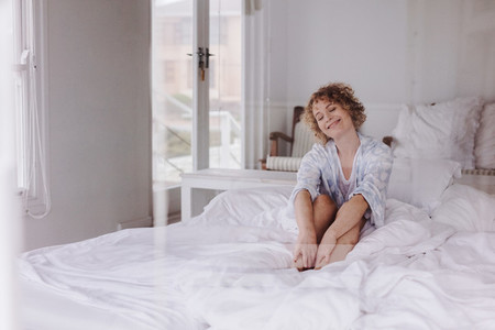 Smiling woman sitting on bed with eyes closed