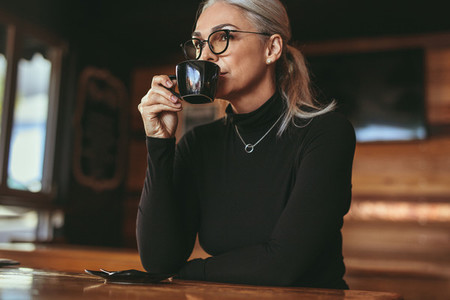 Thoughtful senior woman sitting at cafe drinking coffee