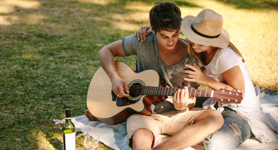 Man sitting in park with his girlfriend playing guitar