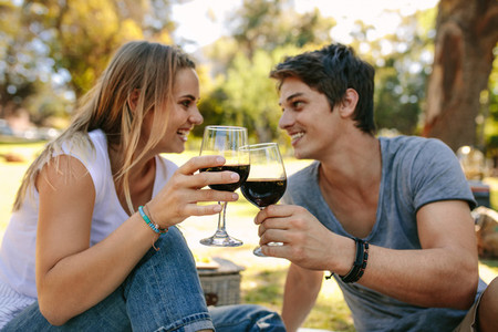 Happy couple on picnic sitting in a park drinking wine