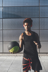 Handsome young afro american basketball player playing with basketball in urban scenery at sunset