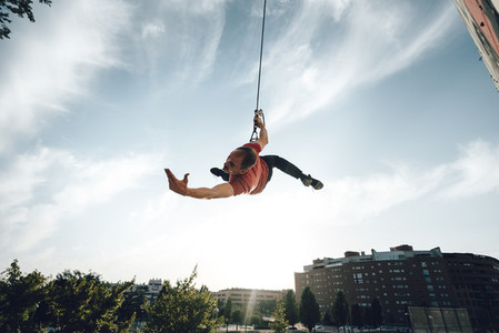 Dancer performing aerial dance hanging on harness on urban scenery at sunset