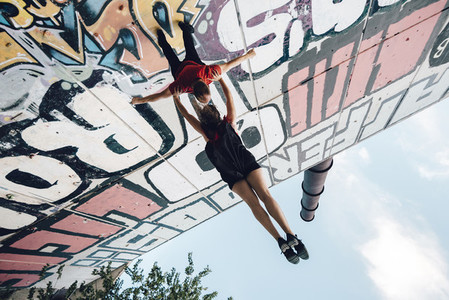 Couple of aerial dancers performing a choreography on urban scenery at sunset against graffitti wall