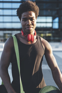 Portrait of young afro man with a basket ball wearing red headphones and a bag waiting friends in urban scenery