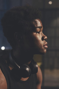 Side view headshot of  young confident afro man wearing black headphones in urban scenery at dusk