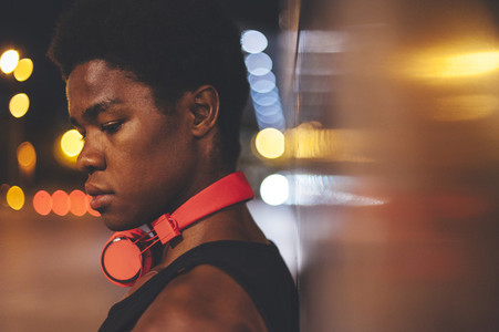 Portrait of  young confident afro man leaning on a wall  wearing red headphones in urban scenery at  night with city lights
