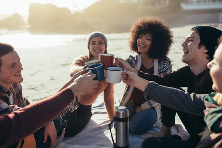 Multi ethnic friends toasting coffee mugs at the beach