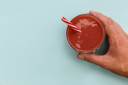 Hand holding red strawberry smoothie drink blue background