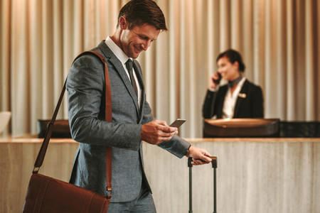 Businessman in hotel hallway with cellphone and luggage