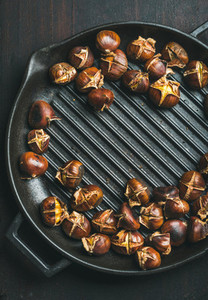 Roasted chestnuts in grilling pan over dark scorched wooden background