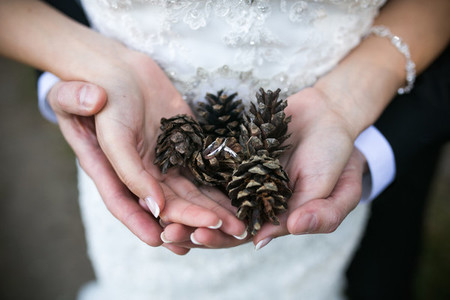 Bride and groom holding wedding rings and autumn leaves in hands