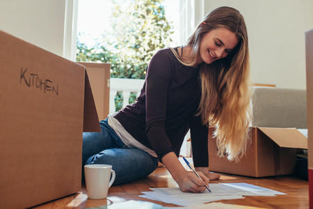 Smiling woman sitting with packing boxes on floor making a list
