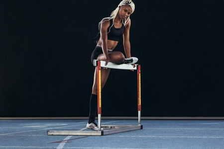 Female sprinter standing beside a hurdle on a running track