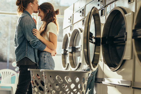 Man kissing his girlfriend on forehead standing in a laundry roo
