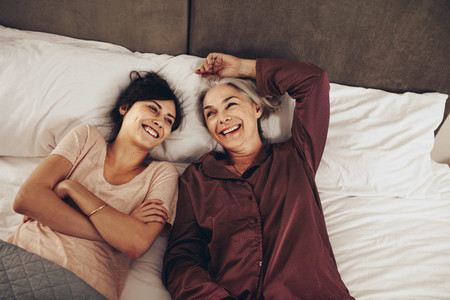 Happy mother and daughter lying on bed together and talking
