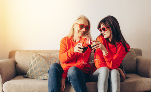 Mother and daughter enjoying wine sitting on couch at home