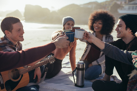Young people toasting with coffee cups on beach