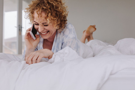 Woman talking over mobile phone lying on bed