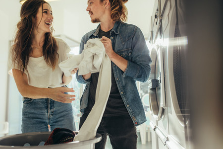 Smiling couple putting clothes in a washing machine together