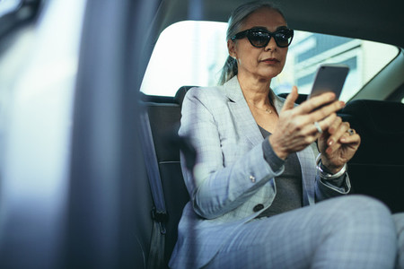 Senior businesswoman traveling by a car using smart phone