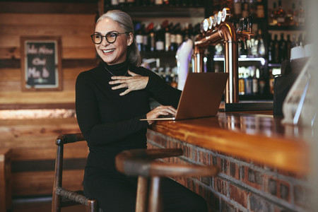 Senior businesswoman sitting at cafe counter with laptop