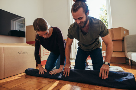 Couple sitting on a carpet and rolling it for packing