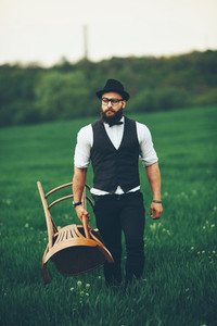 Bearded man carries a chair on the field