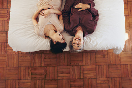 Top view of happy mother and daughter lying on bed and talking