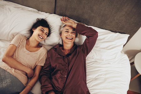 Happy elderly woman lying on bed talking to her daughter
